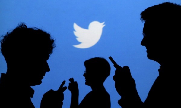 Ações no Twitter Pessoas no celular com a logo do twitter atrás